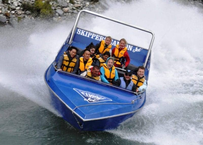 Try out these things not to miss in New Zealand, blue boat speeding through dark grey waters with people in orange life jackets holding on